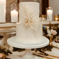 Two-tier smooth style white buttercream cake on white pedestal.