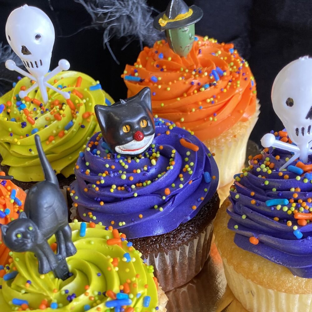 Detail of assorted Halloween cupcakes with colored buttercream frosting and themed toppers.