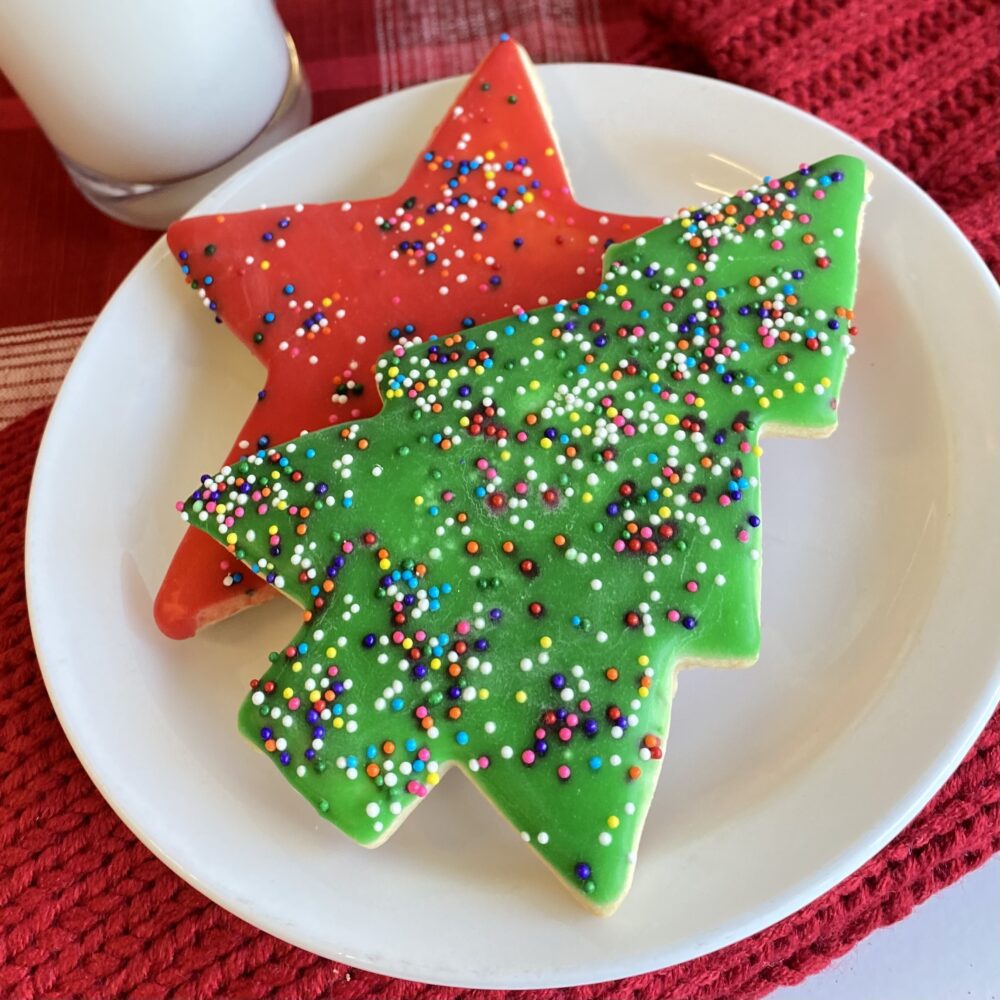A green glazed tree and a red glazed star sugar cookie topped with rainbow nonpareils on a plate.
