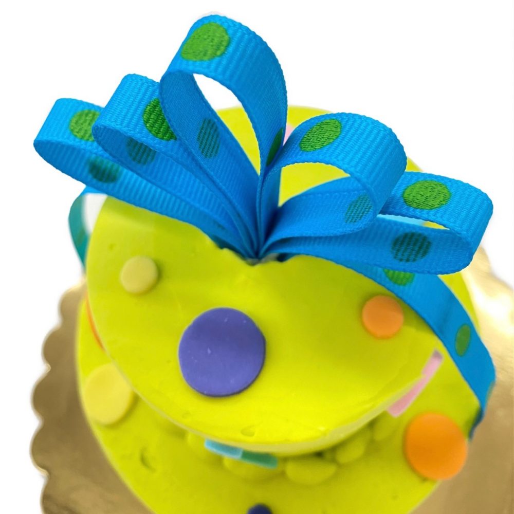 Detail of Itty Bitty Birthday cake in chartreuse with blue ribbon and assorted dots.