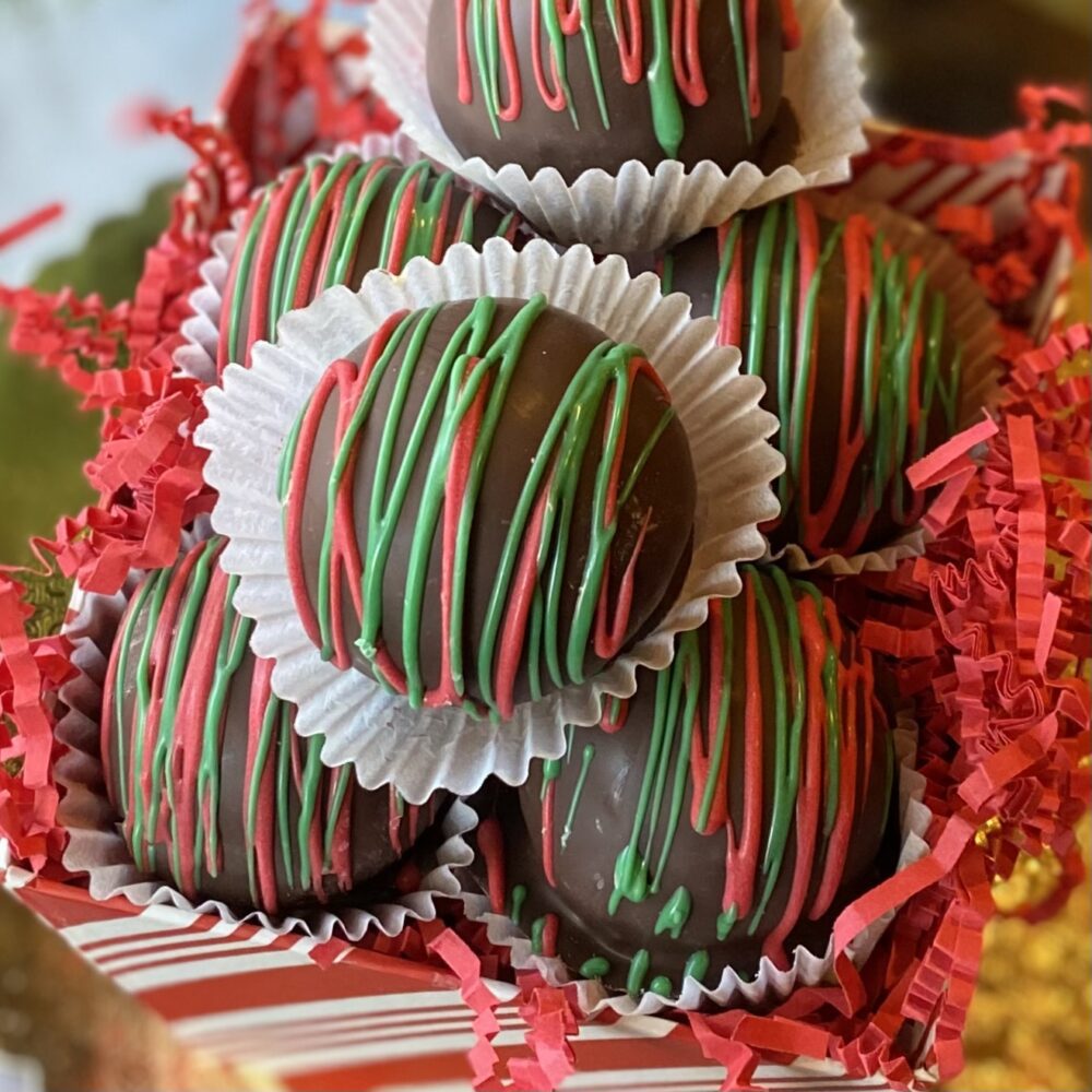 Detail of chocolate-dipped peanut butter balls decorated with green and red chocolate drizzle in a festive gift box.
