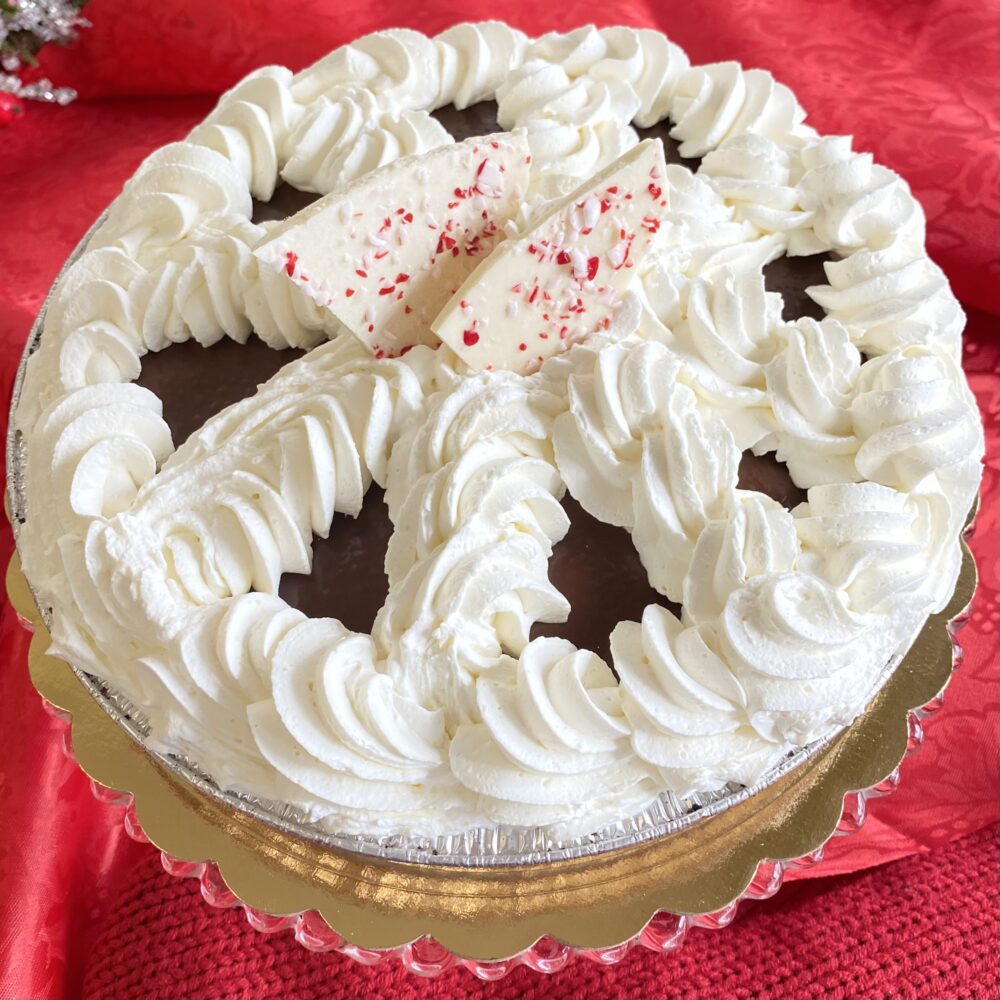 Peppermint pie topped with wheel of piped whipped cream and peppermint bark on a table.