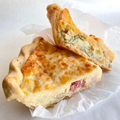 A slice of quiche Lorraine and vegetable quiche on a piece of parchment paper.